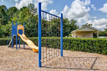 Outdoor playground with slide and climbing wall with wood chips on the ground surrounded by apartment buildings.